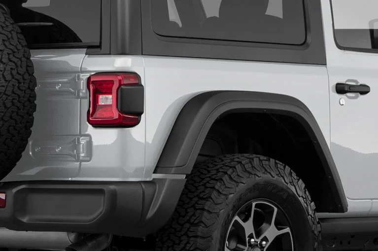 Rear-side view of a silver off-road SUV featuring a rugged black fender flare, all-terrain tire, and a mounted spare tire on the back.