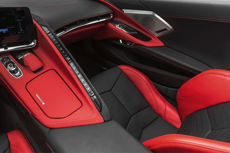 Close-up view of a modern sports car interior with red and black leather seats, a center console with a touchscreen navigation display, and sleek dashboard controls.