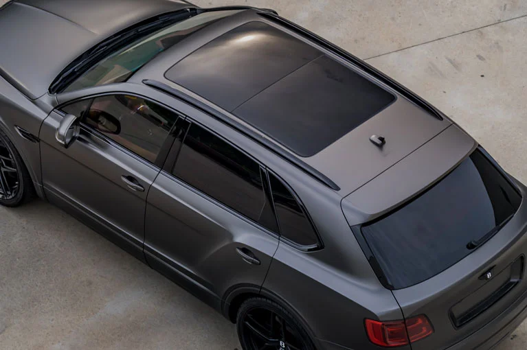 Overhead view of a matte gray luxury SUV with a panoramic sunroof and tinted windows, parked on a concrete surface.