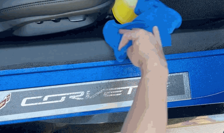 A person cleaning the door sill of a blue Corvette with a microfiber towel in preparation for PPF installation.