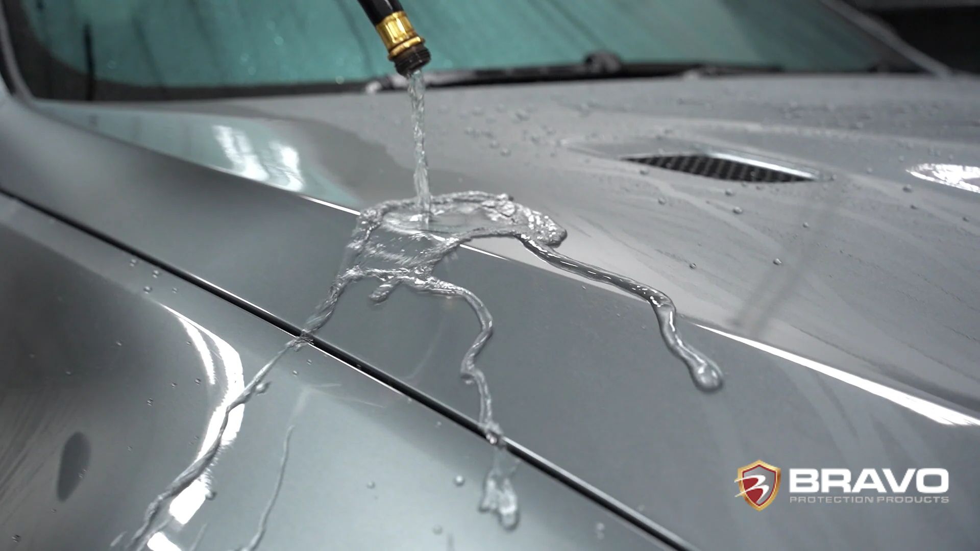 Close-up of water beading and running off a silver car hood treated with ceramic coating, demonstrating its hydrophobic properties.