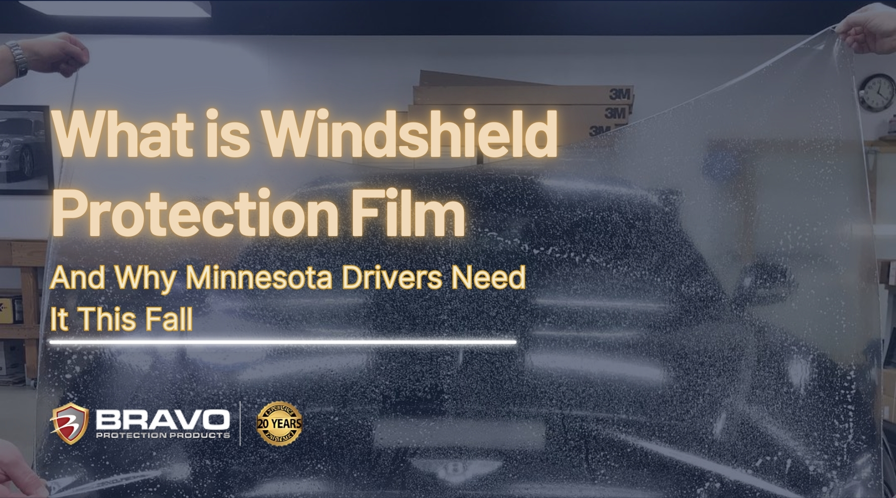 Two people install a clear windshield protection film on a black luxury car inside a Minnesota auto shop, illustrating how the film shields against fall hazards like gravel and temperature shifts. Text on the image reads "What is Windshield Protection Film and Why Minnesota Drivers Need It This Fall."