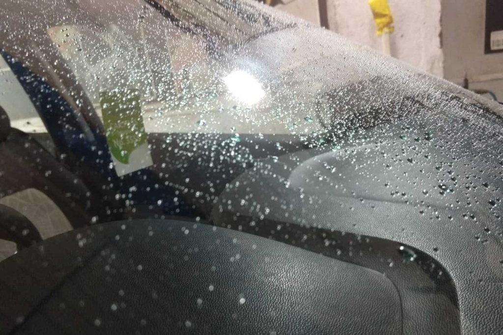 Close-up of a car windshield with water beading on the surface, showing the hydrophobic effect of windshield protection film. The image highlights how the film improves visibility and protects against fall weather conditions in Minnesota.